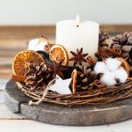 Rustic decor for christmas holiday family dinner. Center piece with white candle, dry orange, cones, cotton. Zero waste eco friendly home decoration. Cozy atmosphere, wooden background. Close up